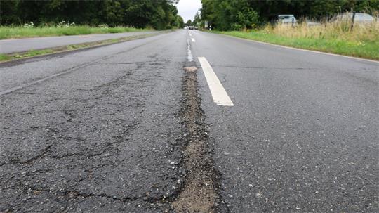 Nahaufnahme einer Straße mit deutlicher Naht zwischen altem, rissigem Asphalt und neuem, glattem Asphalt.