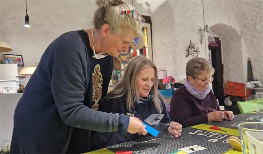 Drei Frauen arbeiten gemeinsam an einem Bastelprojekt mit kleinen Teilen.