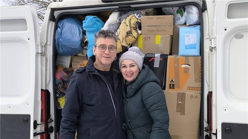 Ein Mann und eine Frau stehen vorm prall gefüllten Transporter, dessen Hintertüren offen stehen. Arm in Arm blicken sie fröhlich in die Kamera.