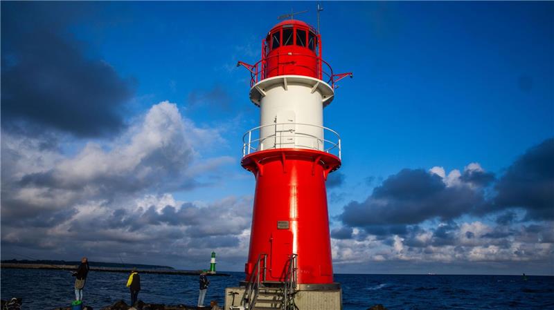 Angler stehen neben dem Leuchtfeuer auf der Ostmole an der Hafeneinfahrt in Warnemünde.