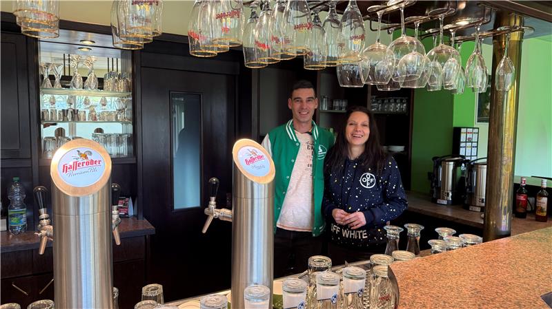 Ein Ehepaar lacht hinter einer Theke in die Kamera