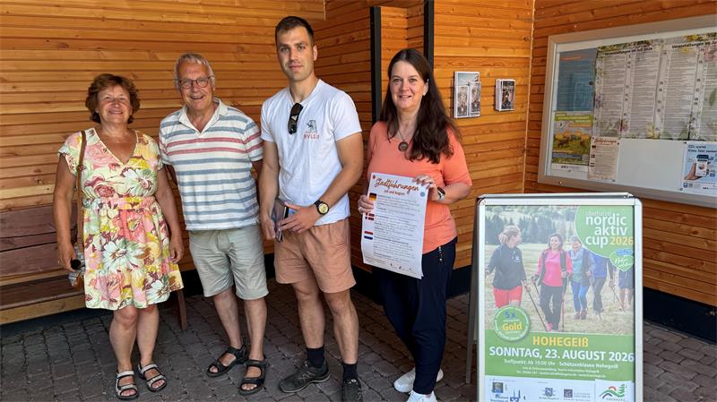 Das Foto zeigt zwei Frauen und zwei Männer, die vor einer Holzwand stehen.