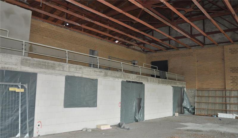 Oker drückt aufs Tempo: Millionenschwere Module rücken an Große, leere Lagerhalle mit freiliegender Deckenstruktur und teilweise abgedeckten Türen und Fenstern