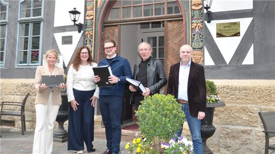 Fünf Personen stehen vor einem Fachwerkhaus mit verzierten Holztüren und Blumenkübeln