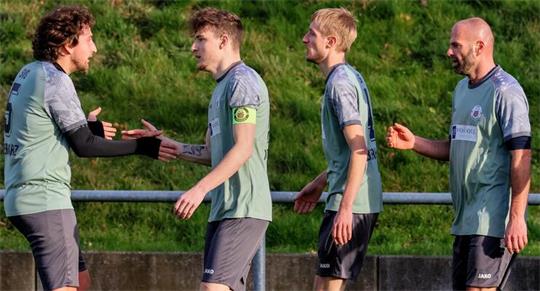 Fußballspieler in grauen Trikots und schwarzen Hosen stehen auf einem Spielfeld und geben sich die Hand
