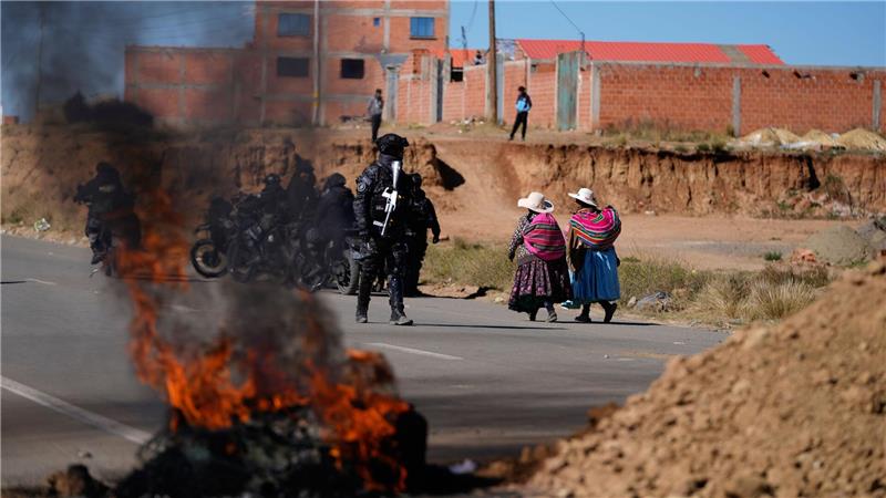 Anwohner gehen an einem Polizisten vorbei, der in Bolivien an einer brennenden Barrikade steht.