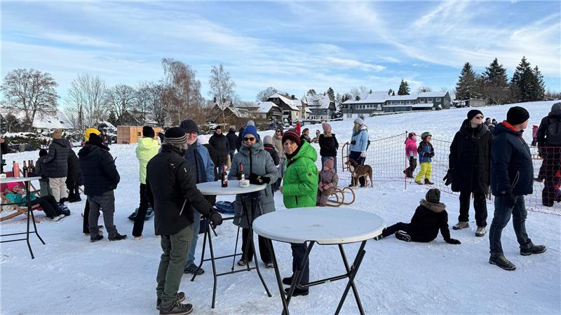 Menschen stehen bei Apres-Ski draußen an Stehtischen und unterhalten sich.