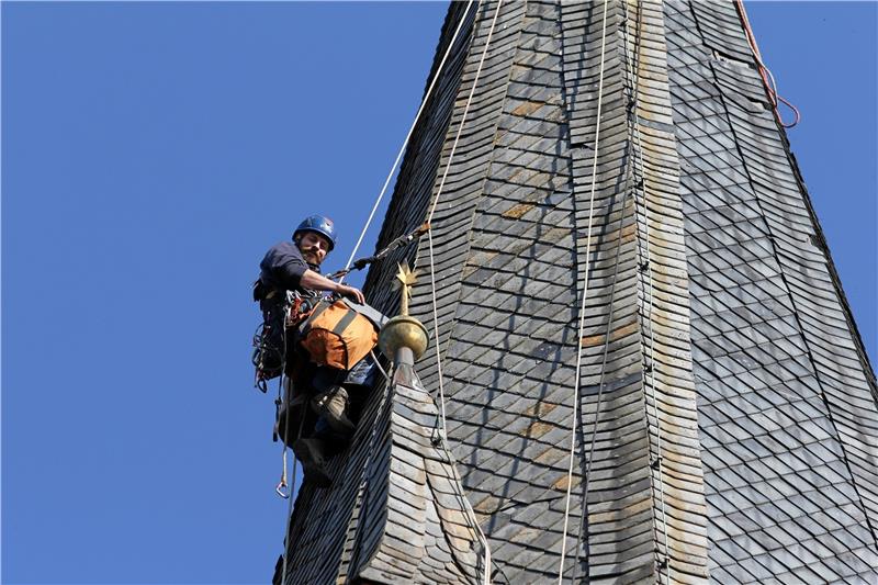 Arbeit in luftiger Höhe: Ein Mitarbeiter der Spezialfirma aus Kassel tauscht die defekten Schiefer-Elemente des Kirchturm-Dachs aus.  Foto: Eggers