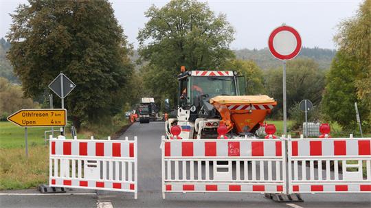 Das Bild zeigt Straßensperrungsschilder. Dahinter sind Bauarbeiter bei der Arbeit. Auch ein Baufahrzeug ist zu sehen.