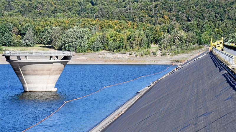 Arbeiten an einem Steilhang – zwischen Überlauf und dem Staudamm schwimmt während der Sanierungsarbeiten im Wasser eine Barriere.