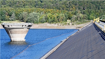 Arbeiten an einem Steilhang – zwischen Überlauf und dem Staudamm schwimmt während der Sanierungsarbeiten im Wasser eine Barriere.