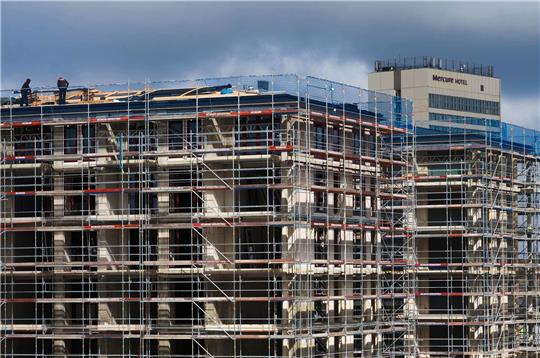 Arbeiter stehen auf dem Dach eines Rohbaus. Der Bundesverband deutscher Wohnungs- und Immobilienunternehmen benötigt mehr Geld für den klimagerechten Neubau.