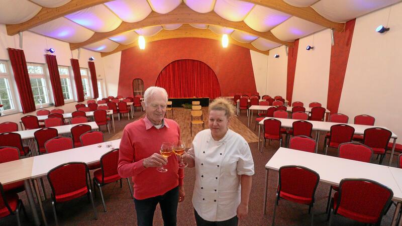 Zwei Personen stehen im Saal und stoßen mit einem Getränk an.