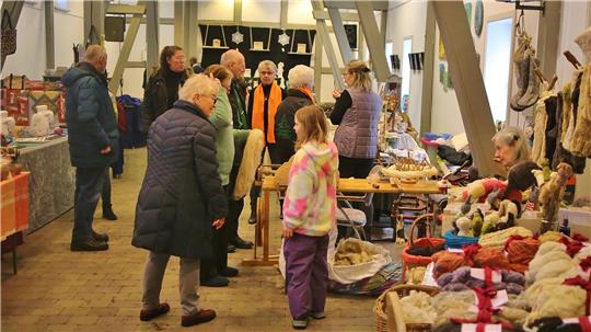 Das Foto zeigt mehrere Menschen in einem Gebäude, die vor Ständen stehen.