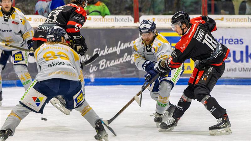 Eishockeyspieler in weiß-gelben und schwarz-roten Trikots kämpfen um den Puck auf dem Eis