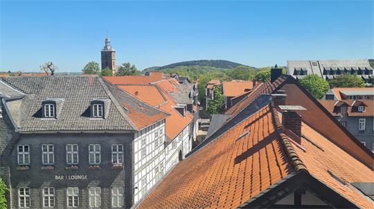 Blick über Dächer mit roten Ziegeln auf Fachwerkhäuser und einen Kirchturm im Hintergrund bei klarem Himmel