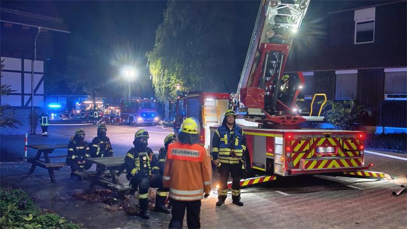 Zimmerbrand bei Bildungseinrichtung in Seesen: 23 Personen evakuiert Feuerwehrmänner beobachten das Einsatzgeschehen, die Drehleiter ist ausgefahren