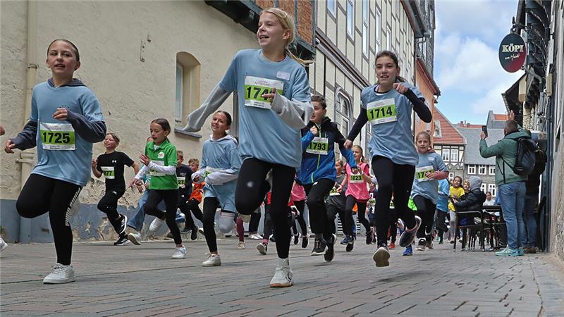 Läufergruppe mit Startnummern läuft auf gepflasterter Straße in Altstadt mit Fachwerkhäusern im Hintergrund.