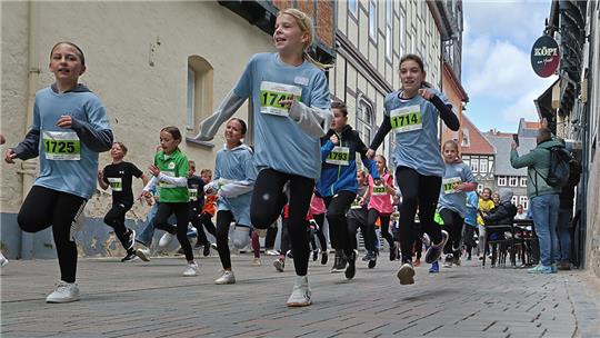 Läufergruppe mit Startnummern läuft auf gepflasterter Straße in Altstadt mit Fachwerkhäusern im Hintergrund.