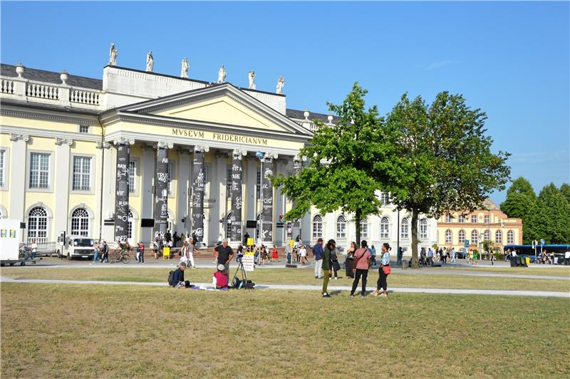 Jimmie Durhams Gruß von der Documenta fifteen Auch die Säulen des Fridericianum werden zum Kunstwerk der Ausstellung und laden mit ihren Botschaften zum Verweilen ein. Davor hat sich Kaiserringträger Joseph Beuys mit der ersten und der letzten seiner 7000 Eichen verewigt. Foto: Meyer-Zurwelle