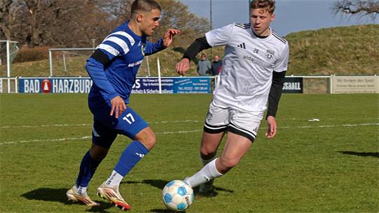 Zwei Fußballspieler in Aktion auf dem Spielfeld, einer in blauem Trikot mit der Nummer 17, der andere in weißem Trikot, beide schauen konzentriert auf den Ball am Boden