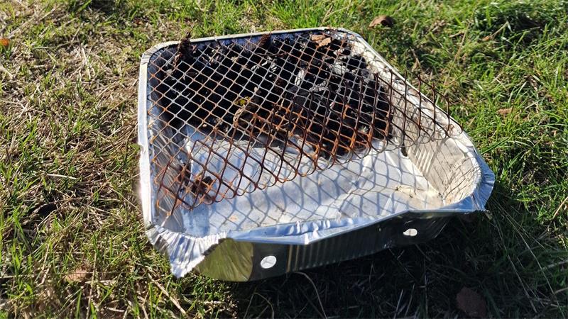 Ein benutzter Einweggrill auf einer grünen Wiese.