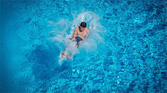 Das Bild zeigt einen jungen Mann, der rückwärts im Wasser eines Swimmingpools einschlägt. 
