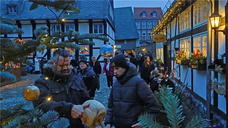 Weihnachtsmarkt mit Fachwerkhäusern, geschmückten Tannenbäumen und mehreren Menschen in Winterkleidung am Abend.