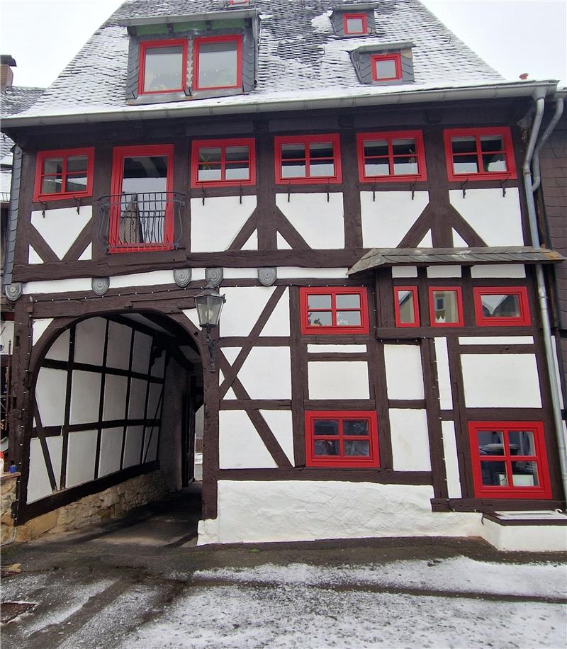 Fachwerkhaus mit roten Fensterrahmen, verschneitem Dach und Durchfahrt unter dem Gebäude.