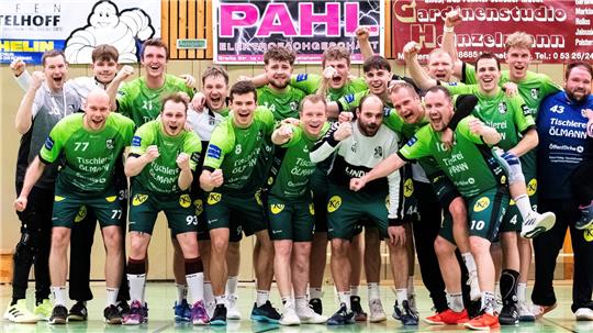 Gruppenfoto einer Handballmannschaft in grünen Trikots in einer Sporthalle vor Werbebannern