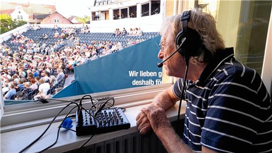 Audiodeskriptor Paul Beßler am Fenster mit Blick auf die Tribüne/Bühne.
