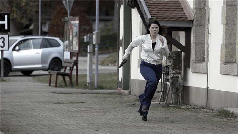 Eine Frau rennt mit der Waffe in der Hand über den Bahnsteig.