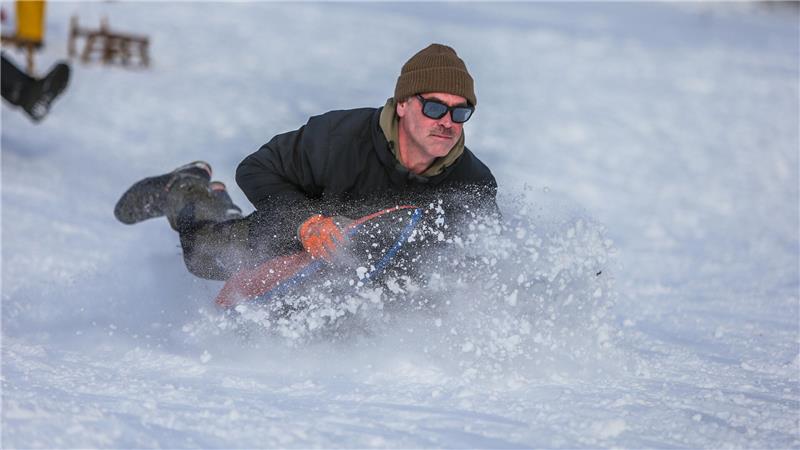 Ein Mann rutscht mit einem Schlitten den Hang hinab.