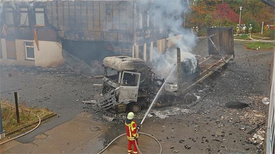 Feuerwehrleute löschen einen brennenden Lastwagen, der vor einem Gebäude steht.