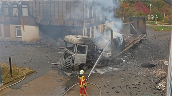 Feuerwehrleute löschen einen brennenden Lastwagen, der vor einem Gebäude steht.