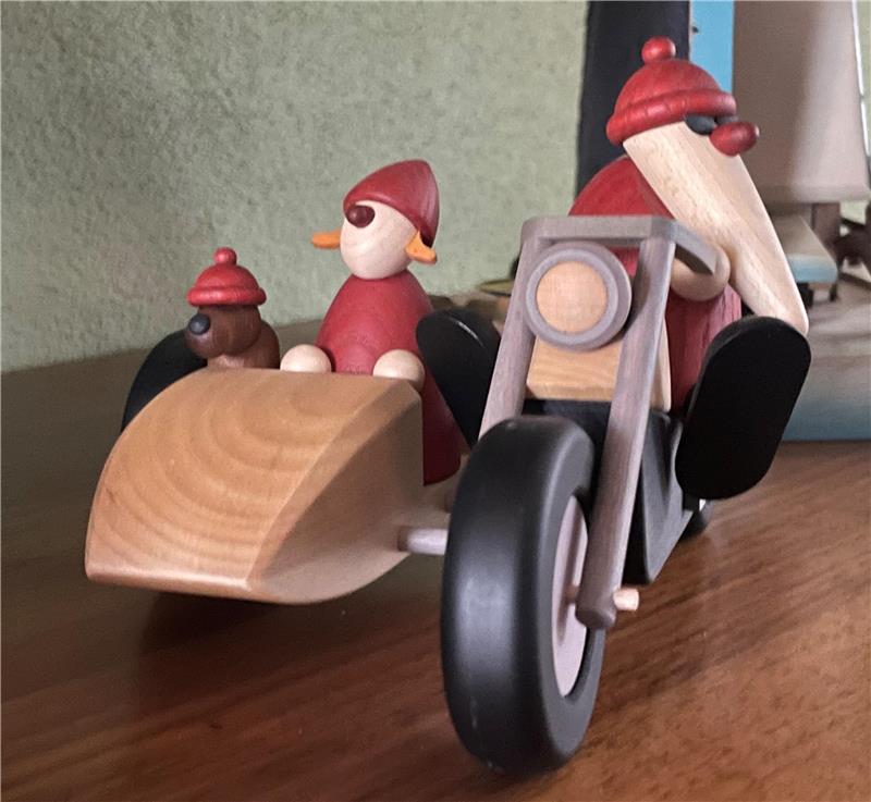 Heiße Geschenktipps: Kleine weißbärtige Rotnasen aus Sachsen Holzspielzeug-Motorrad mit Beiwagen, darin zwei kleine Figuren mit roten Mützen, auf braunem Holztisch.