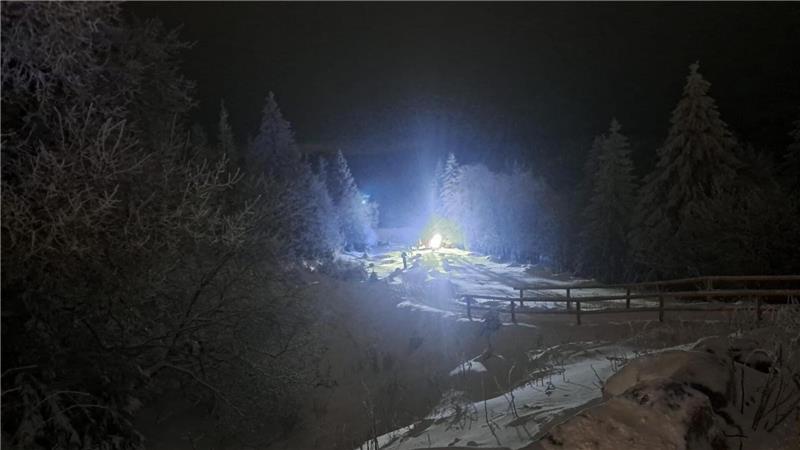 Ein Licht scheint zwischen einigen Bäumen auf einem verschneiten Hügel.