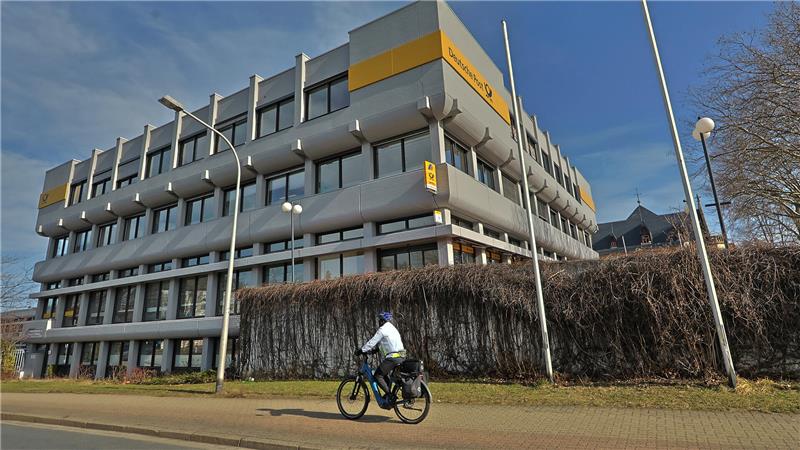 Mehrstöckiges Bürogebäude mit gelbem Schriftzug und Fahrradfahrer auf Straße davor