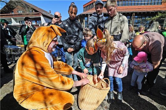 Ein Mann im Osterhasenkostüm lässt die um ihn herumstehenden Kinder in seine Tasche greifen.