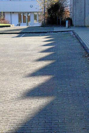 Das Dach der Sporthalle wirft Schatten auf einen Parkplatz.
