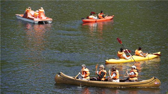 Das Bild zeigt junge Menschen, die in Kajaks und Tretboten Wassersport treiben. 