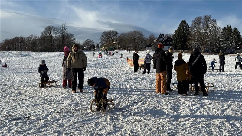Familien stehen mit Schlitten auf dem verschneiten Berg.