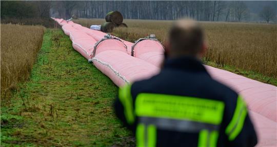 Auf einem Feld liegt ein Teil von einem mobilen Deich, welcher mit Wasser befüllt ist.