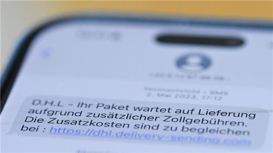 Auf einem Smartphone ist eine Betrugs-SMS zu lesen, in der Kriminelle ein Paket ankündigen und dafür Zollgebühren einfordern. 