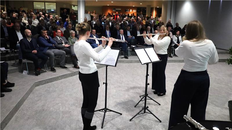 Drei Mädchen stehen im Vordergrund und spielen Querflöte vor einer großen Menschenmasse.