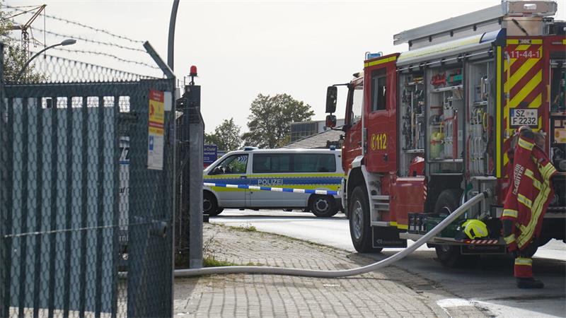 Ein Polizeifahrzeug, sowie ein Feuerwehrlöschfahrzeug stehen vor einem Zaun eines Firmengeländes.