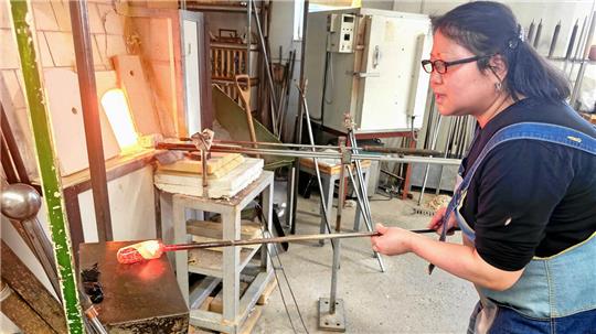  Glasmacherei Emi Yamamoto in der Werkstatt, beim Formen eines heißen Glasklumpens.