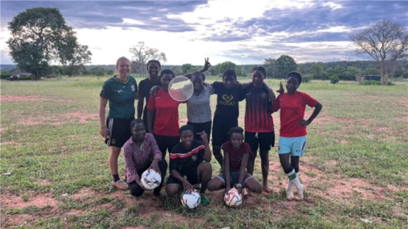 Goslarer CvD-Gymnasium erläuft 8500 Euro für „Girls in Action“ Gruppe von neun Personen auf einer Wiese, einige halten oder sitzen neben Fußbällen, im Hintergrund Bäume und bewölkter Himmel.