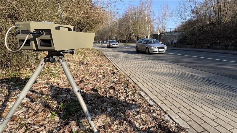 Geschwindigkeitsmessgerät auf einem Stativ am Straßenrand neben einer Straße mit zwei vorbeifahrenden Autos