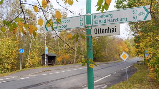 das Bild zeigt ein Straßenschild und im Hintergrund die Landesstraße 501 sowie zwei Bushaltestellen.